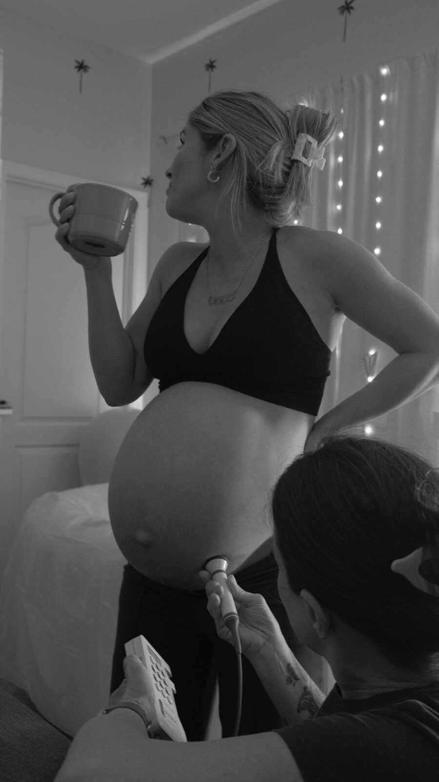 An expecting mother sips from a mug while Rhonda listens to baby's heartbeat
