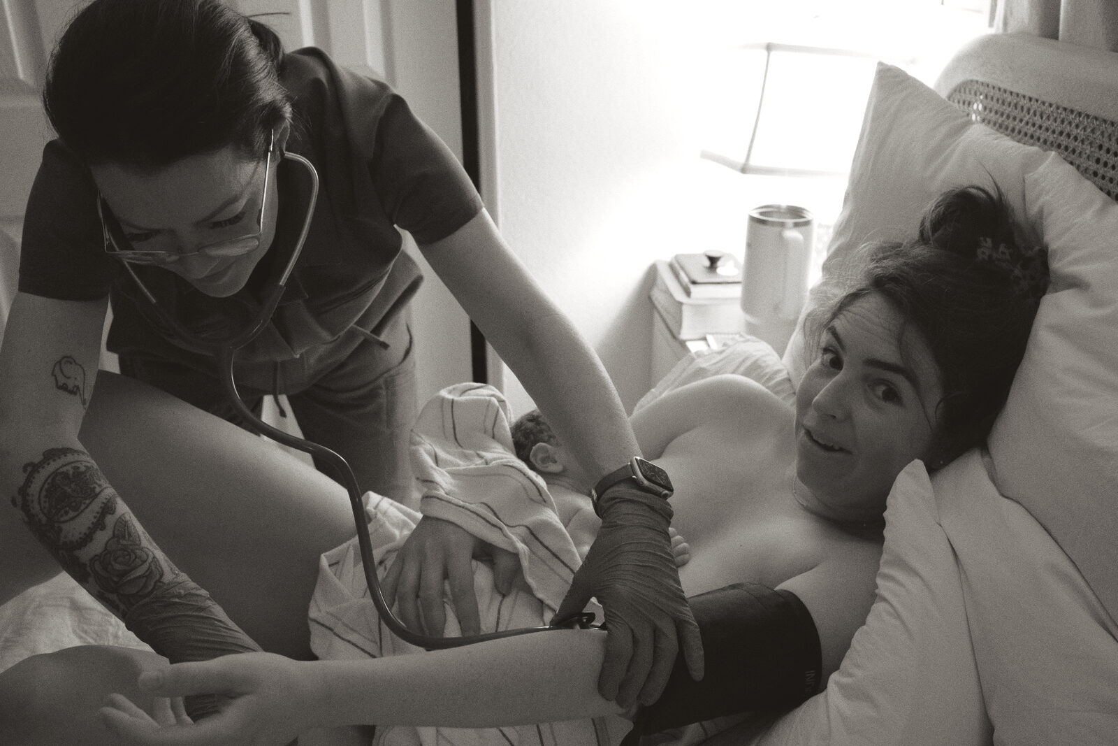 Rhonda checking a mother's blood pressure with her newborn resting close during a tender postpartum visit