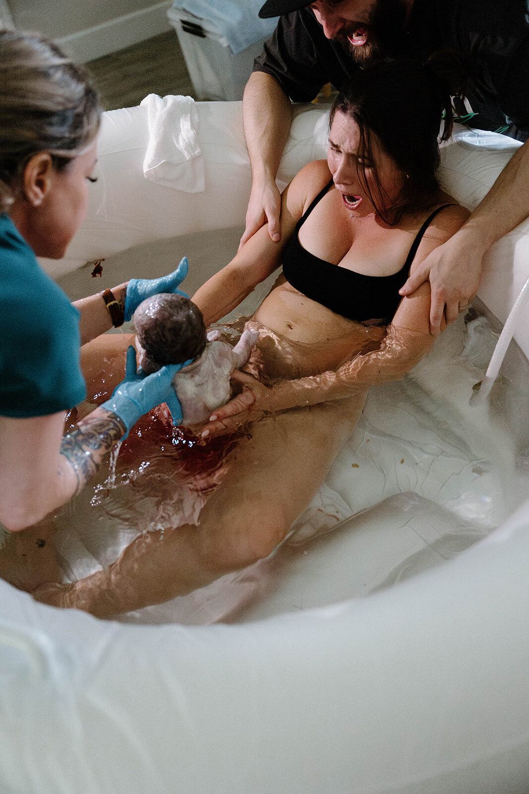 Rhonda catching a baby at the moment of a water birth as the mother reaches for her newborn